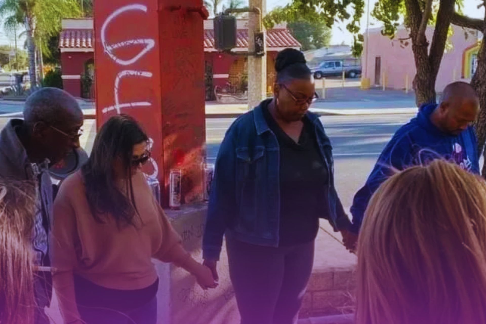 A group of people are holding hands and praying on the sidewalk.