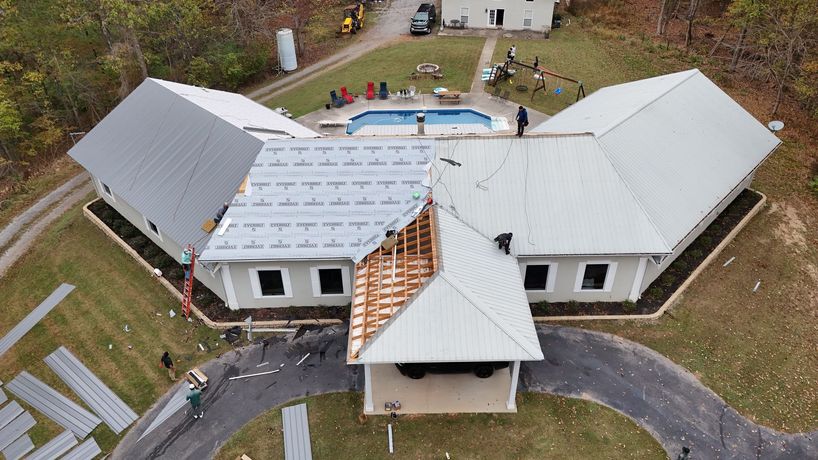 Aerial view of a house undergoing metal roof installation, with a partly exposed roof section, equipment, and a pool.