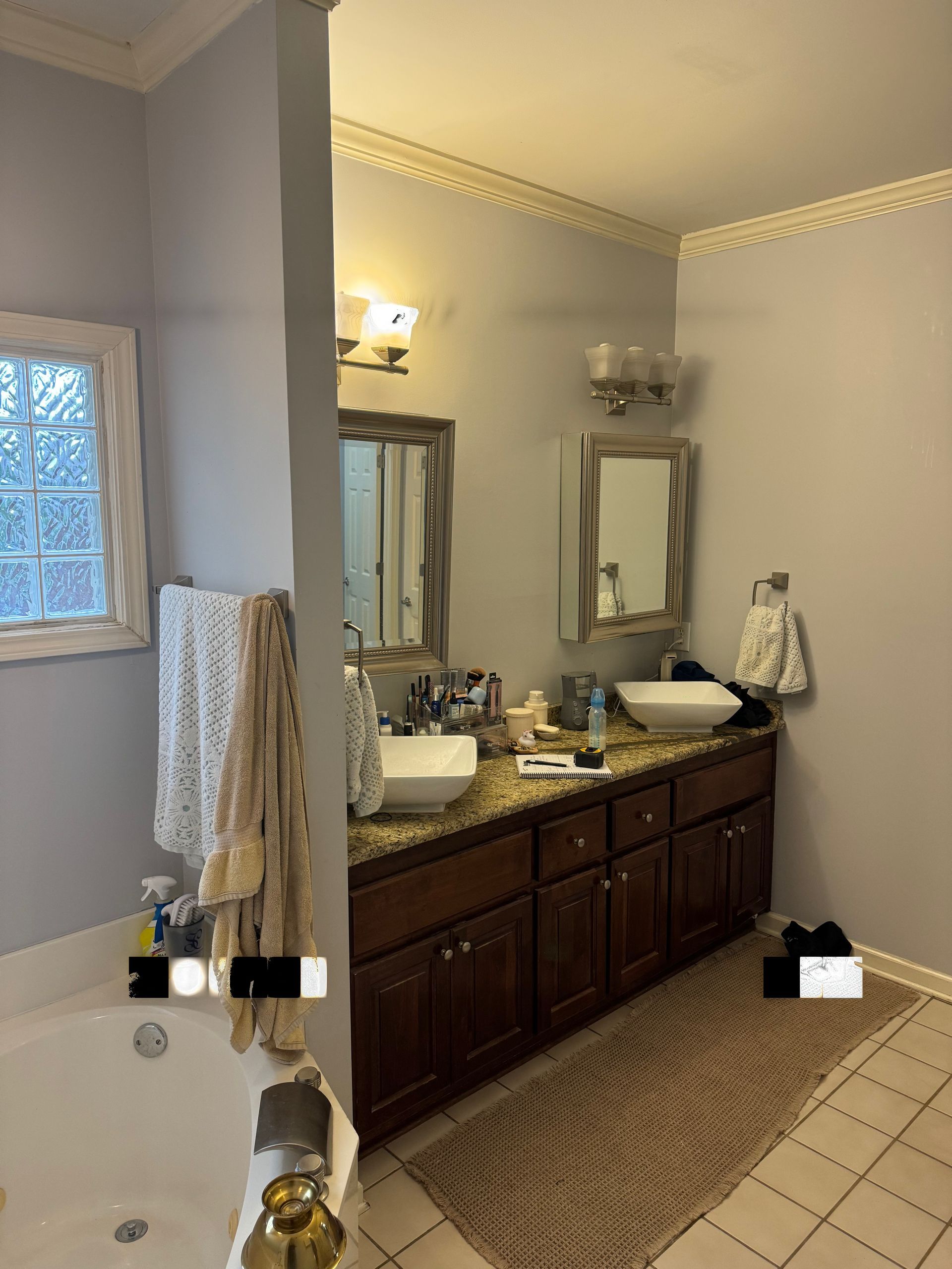 A bathroom featuring dark wood cabinets, dual vessel sinks, a granite countertop, and a large soaking tub.