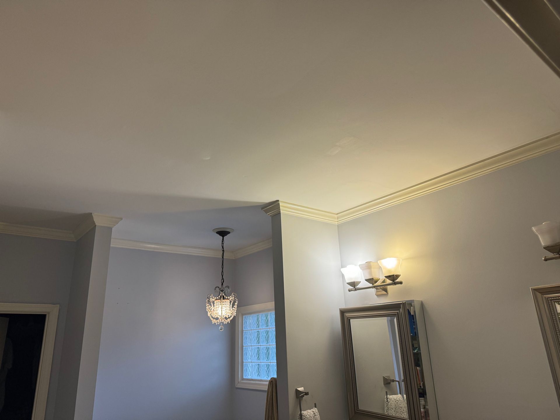 A bathroom interior with white crown molding, light blue walls, a hanging pendant light, and a wall-mounted vanity mirror.