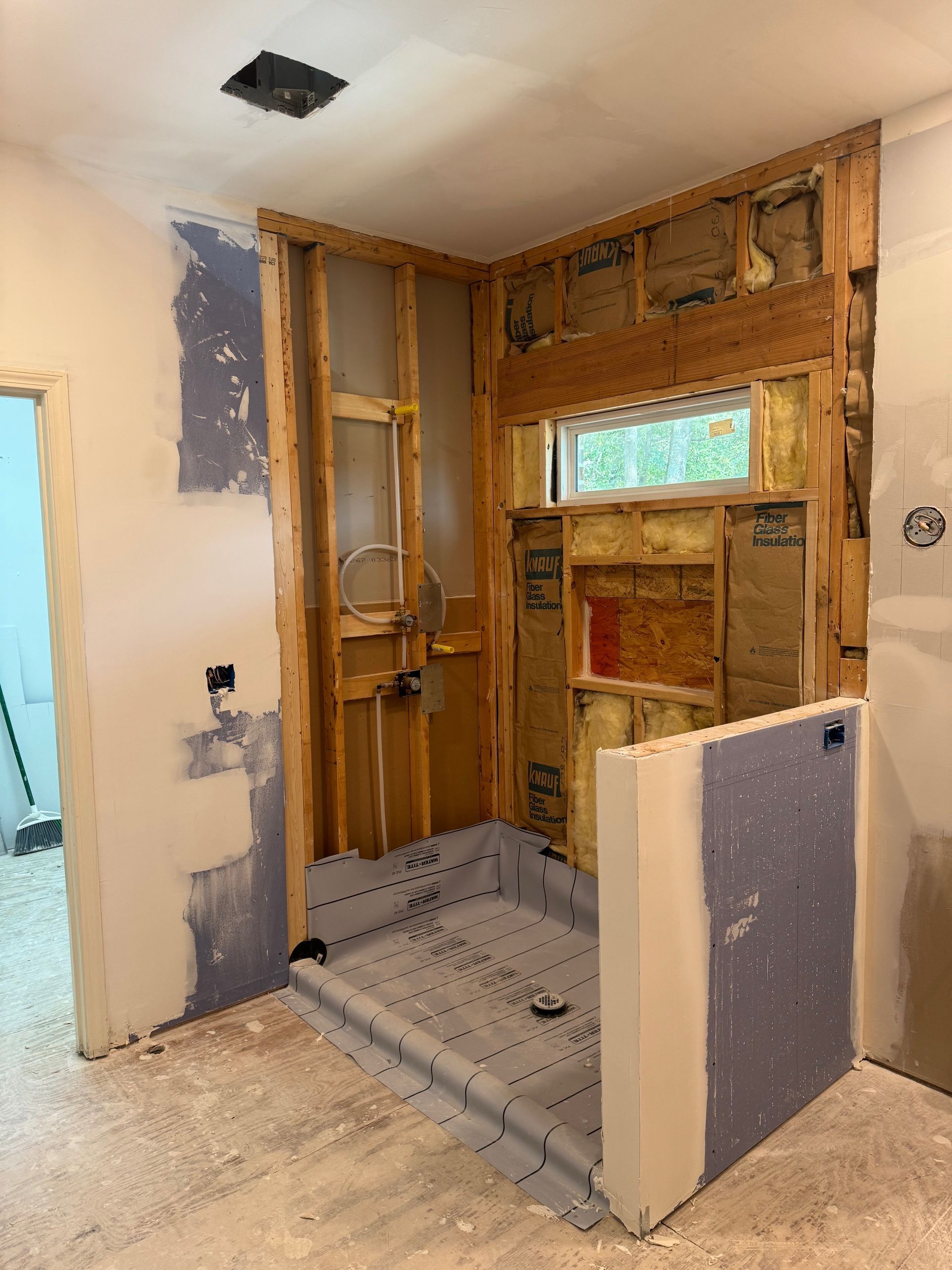 A bathroom shower undergoing renovation with exposed wooden studs, tiled shower pan, and unfinished drywall.