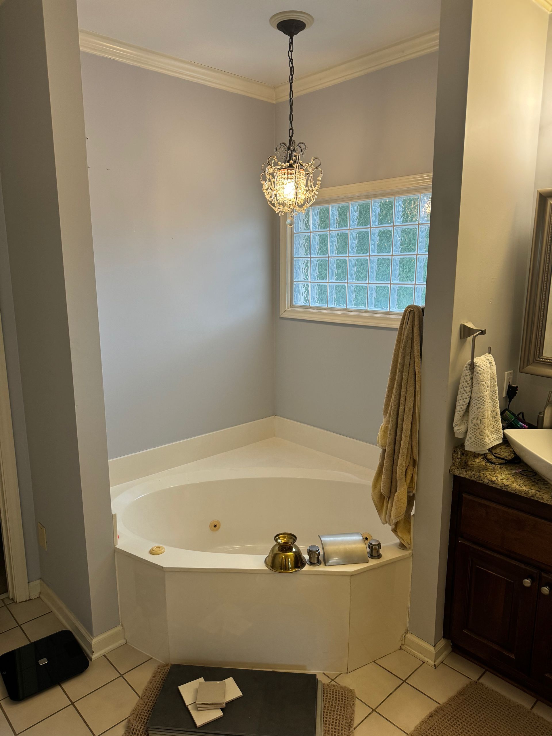 A corner soaking tub with light blue walls and a hanging pendant light below a glass block window in a bathroom.