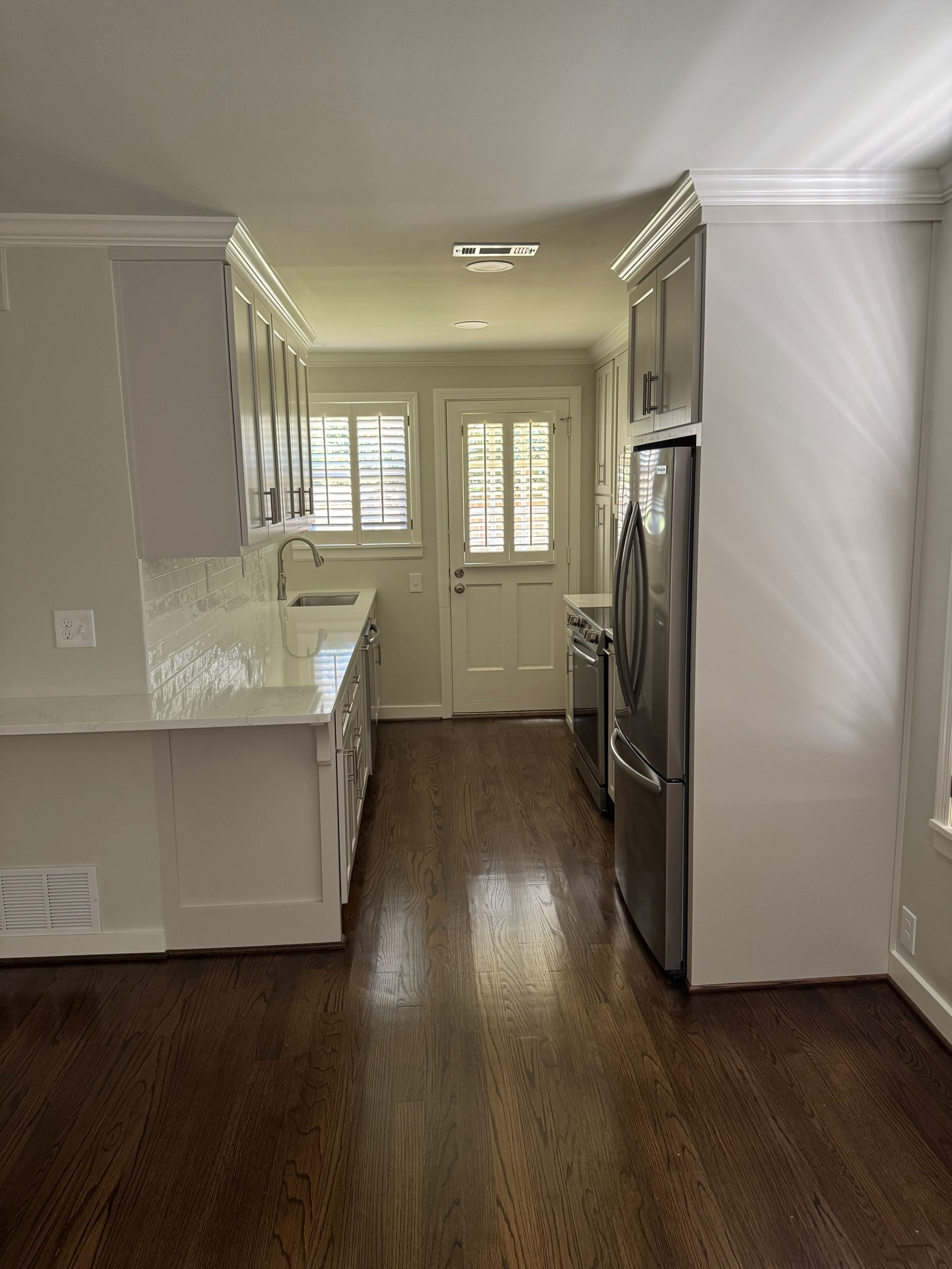 A modern kitchen with white cabinets, stainless steel appliances, dark wood flooring, and a door leading to the outside.