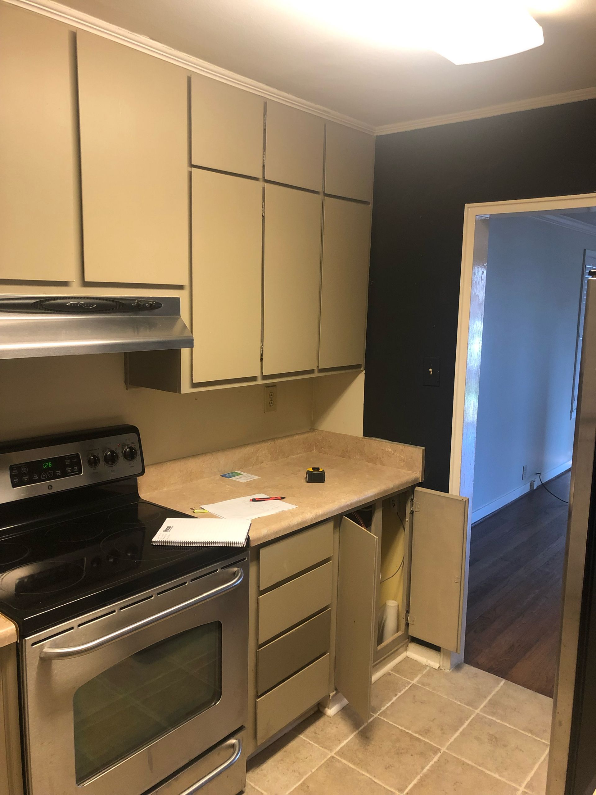 A kitchen view with tan cabinets, a stainless steel stove, speckled countertops, and a doorway leading to another room.