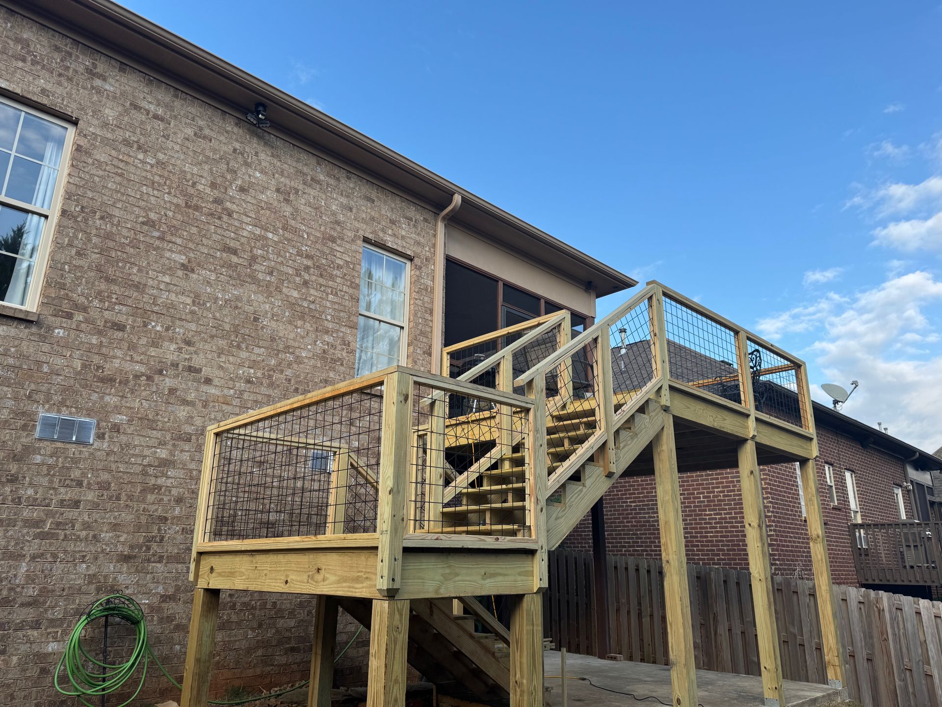 A newly built wooden deck and staircase attached to the back of a brick house under a clear blue sky.