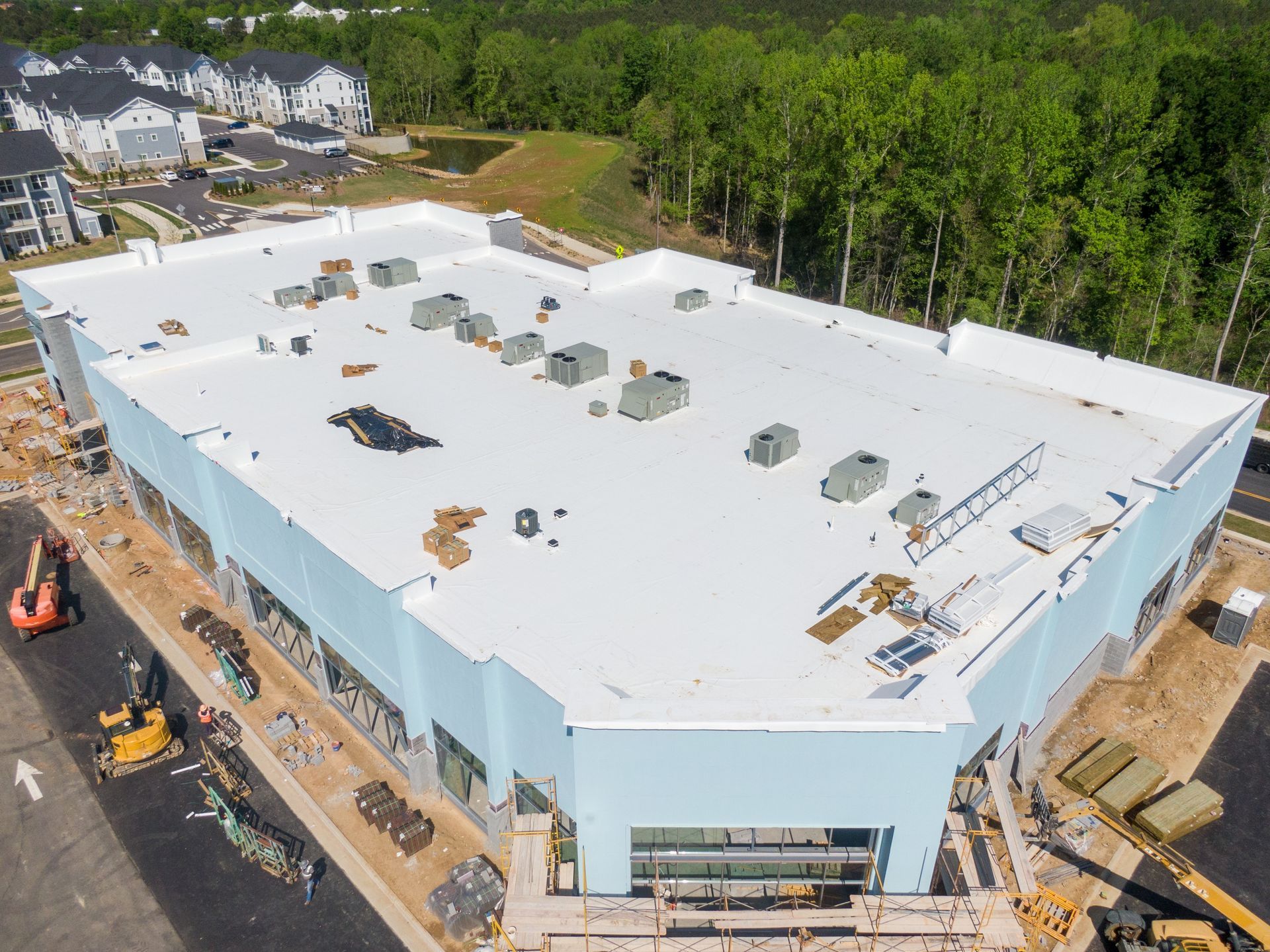 An aerial view of a new commercial building with a white roof under construction, surrounded by construction equipment.