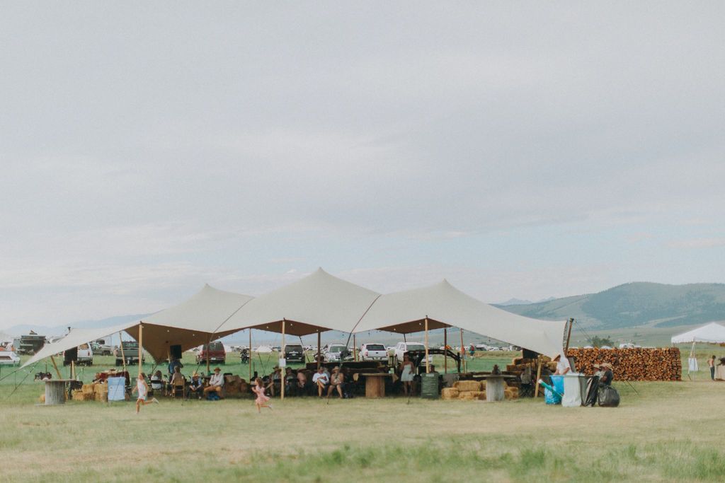 A group of people are sitting under tents in a field.