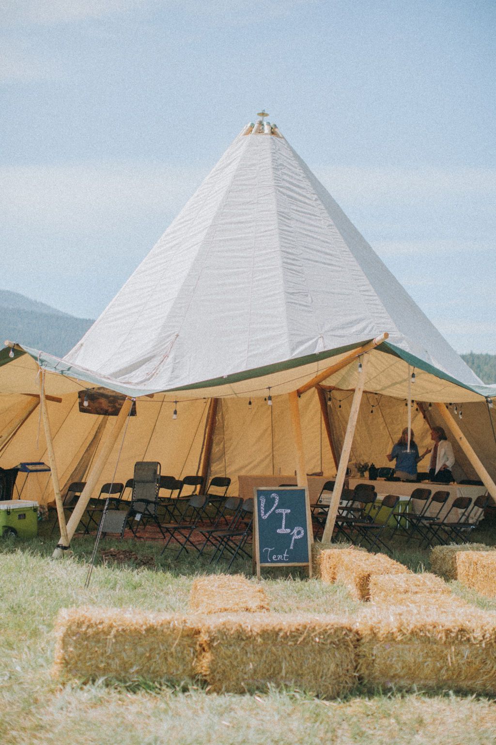 A large tent is sitting in the middle of a field next to hay bales.
