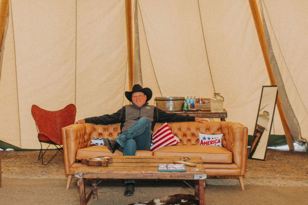 A man in a cowboy hat is sitting on a couch in a tent.