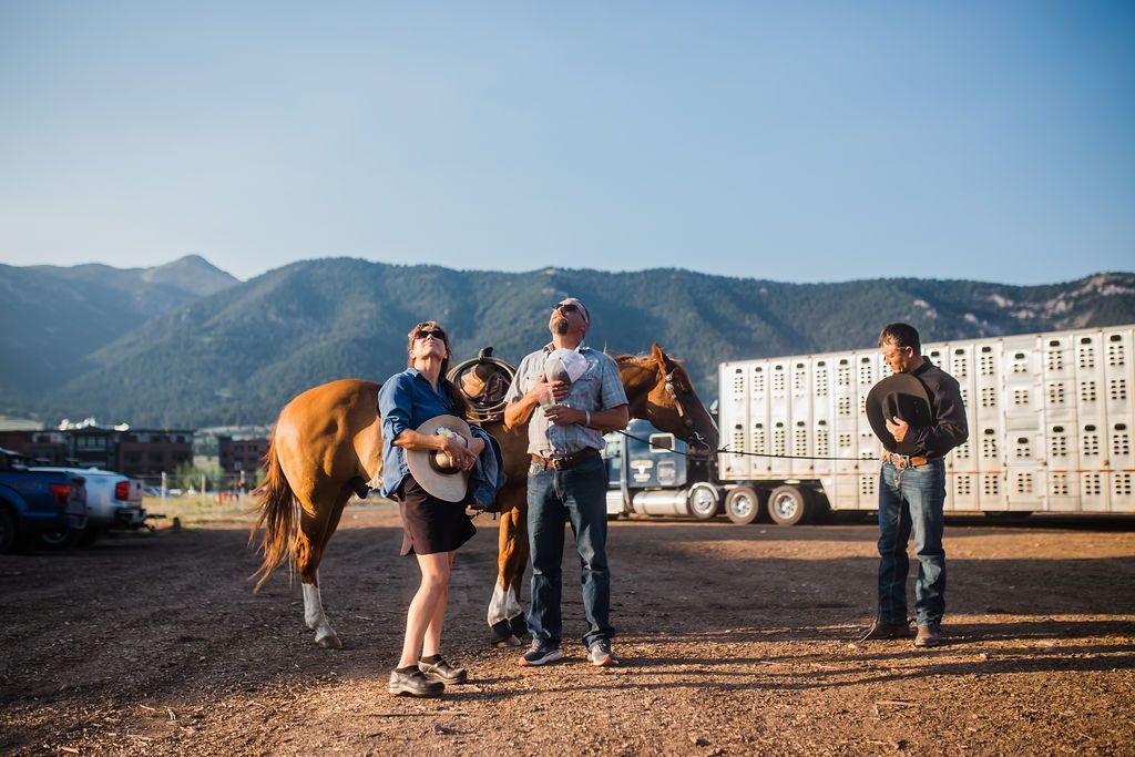 A group of people standing next to horses in a dirt field.