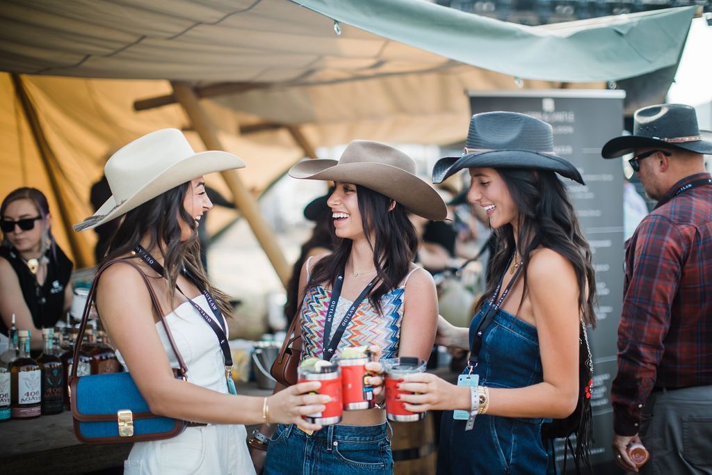 Three women wearing cowboy hats are standing next to each other holding drinks.