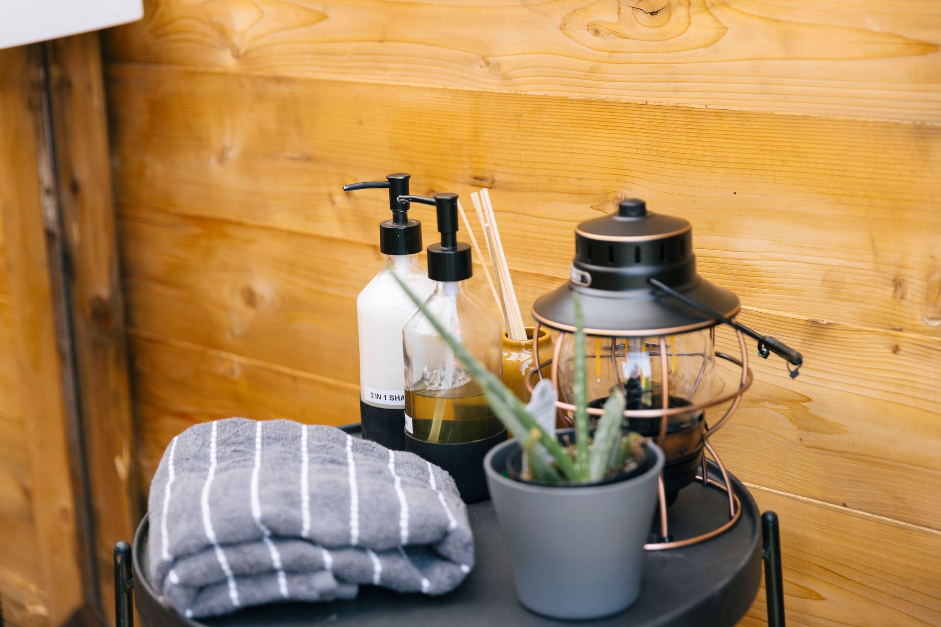 A table with a towel , soap dispensers , a potted plant and a lantern on it.