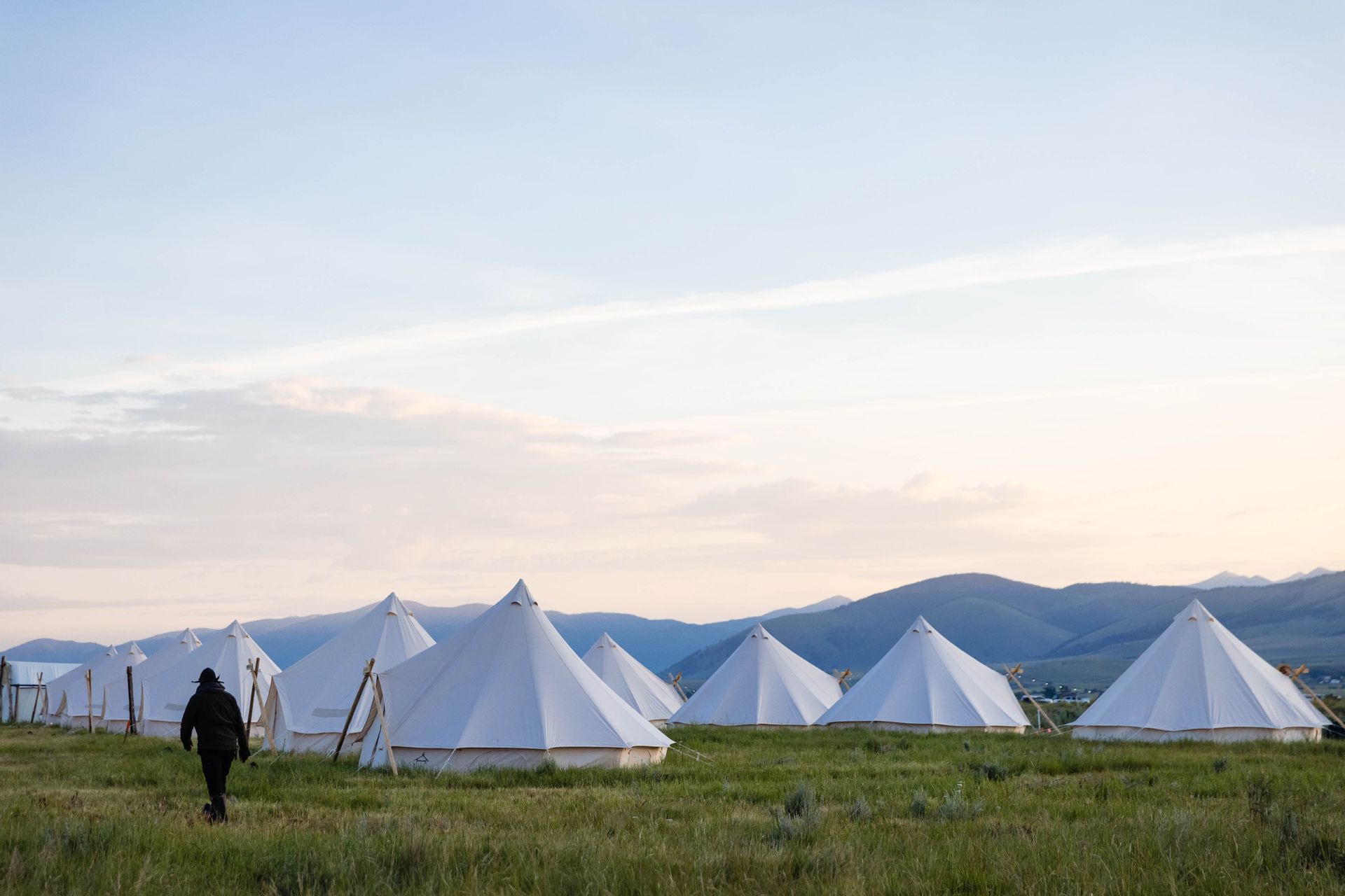 A person is walking in a field of tents with mountains in the background.
