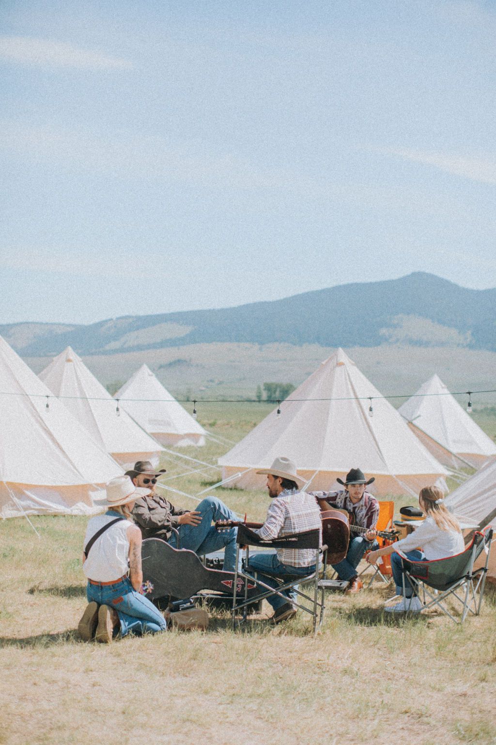 A group of people are sitting around a campfire in a field.