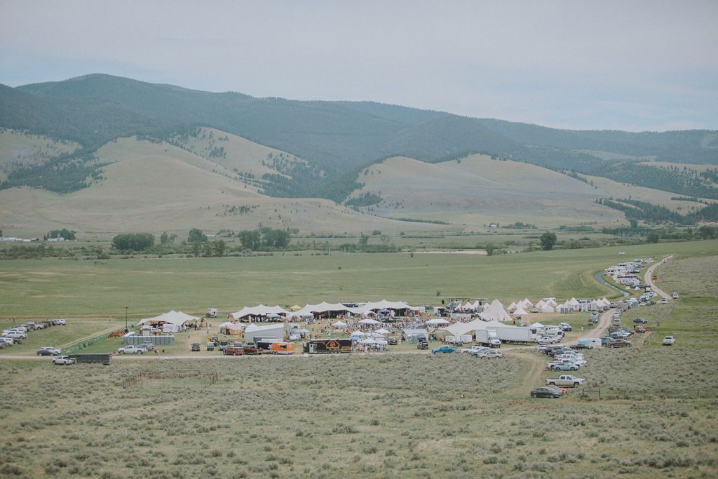A large group of people are gathered in a field with mountains in the background.