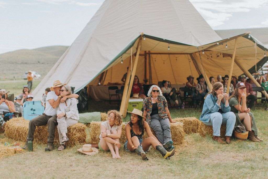 A group of people are sitting on hay bales in front of a tent.