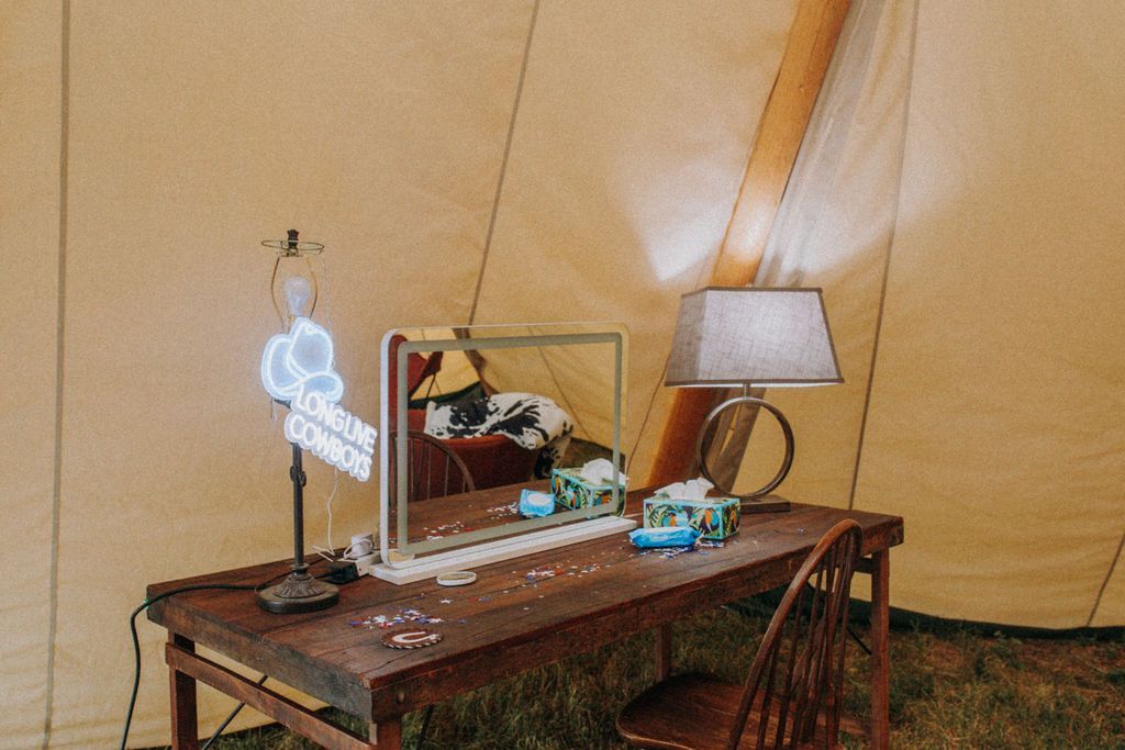 A wooden table with a mirror and a lamp in front of a tent.
