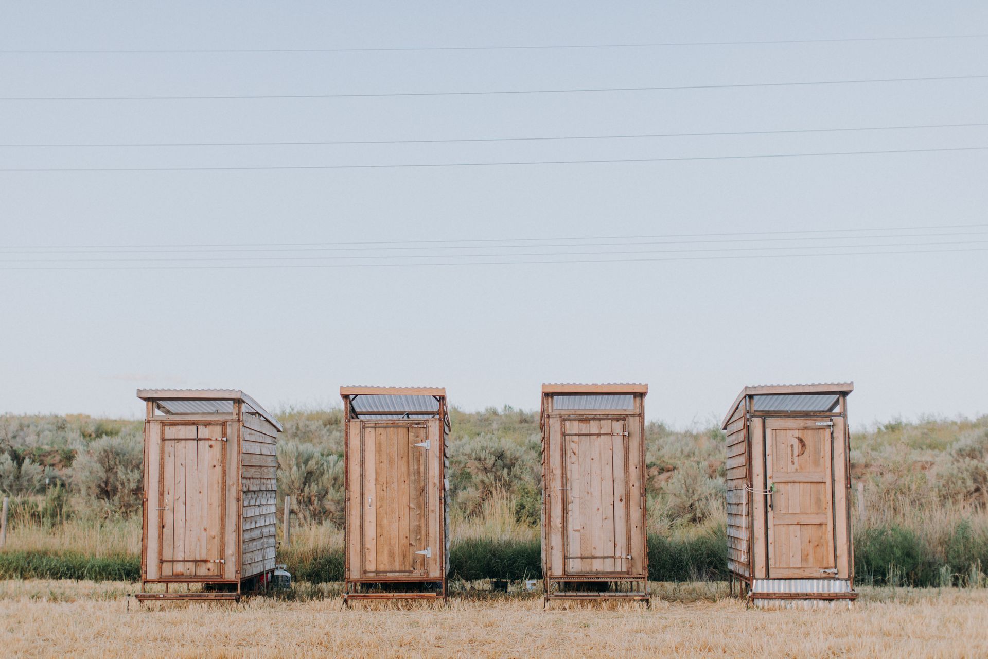 A row of wooden toilets are lined up in a field.