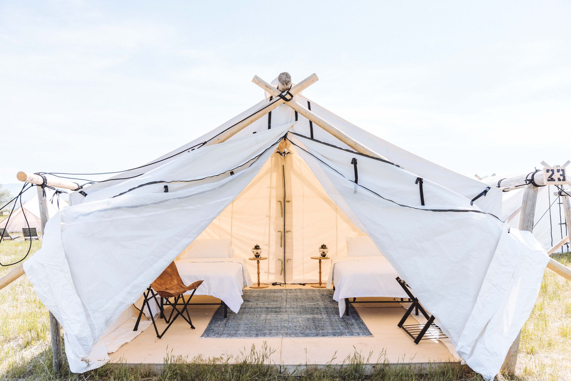 A white tent with two beds and a chair in a field.