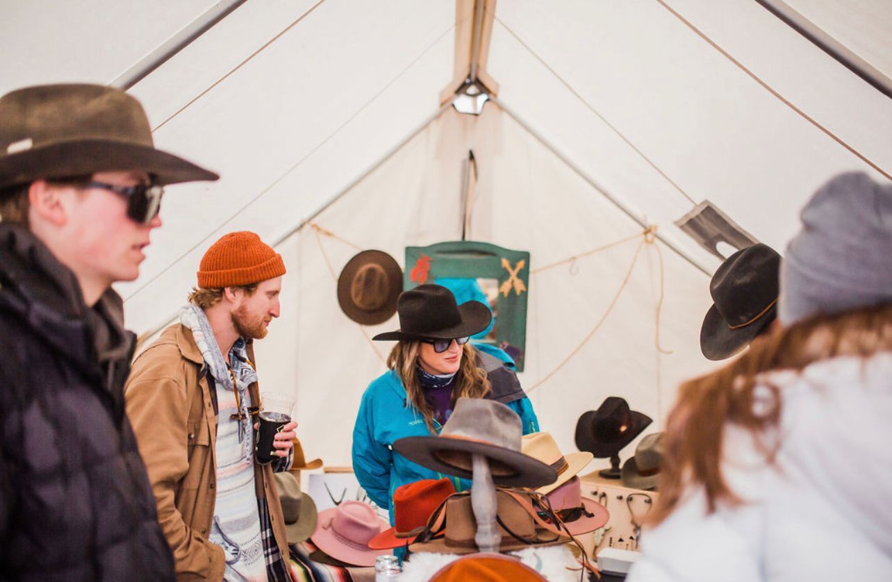 A group of people are standing in a tent looking at hats.