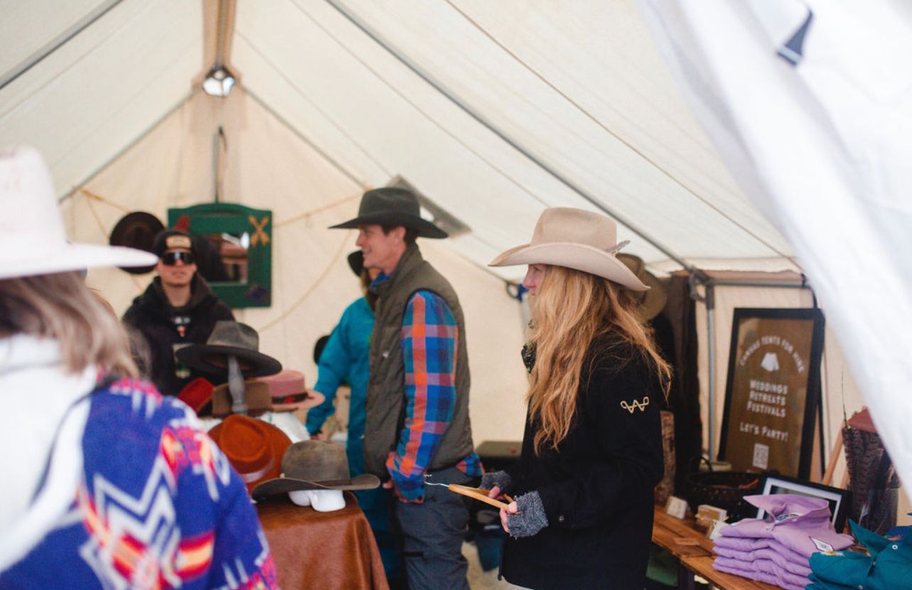 A group of people are standing in a tent looking at hats.