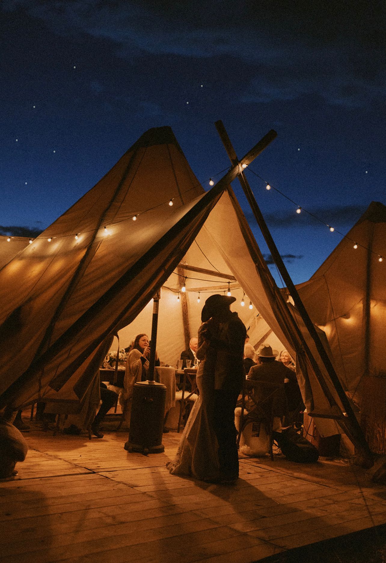 A bride and groom are dancing in a tent at night.