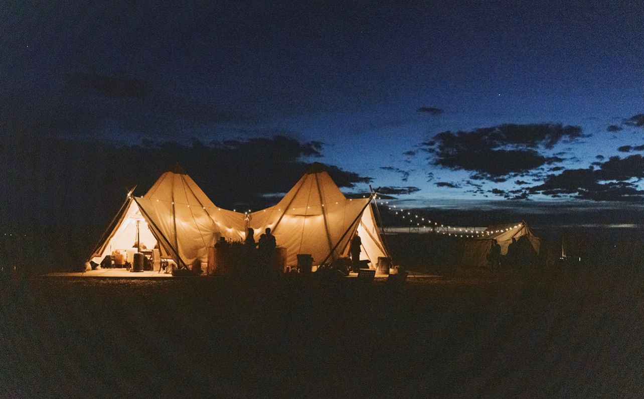 A group of tents are lit up at night in a field.