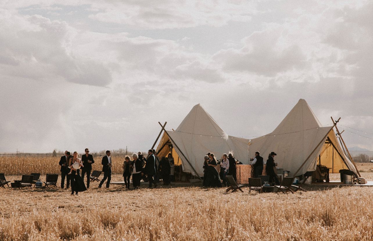 A group of people are standing in a field in front of tents.