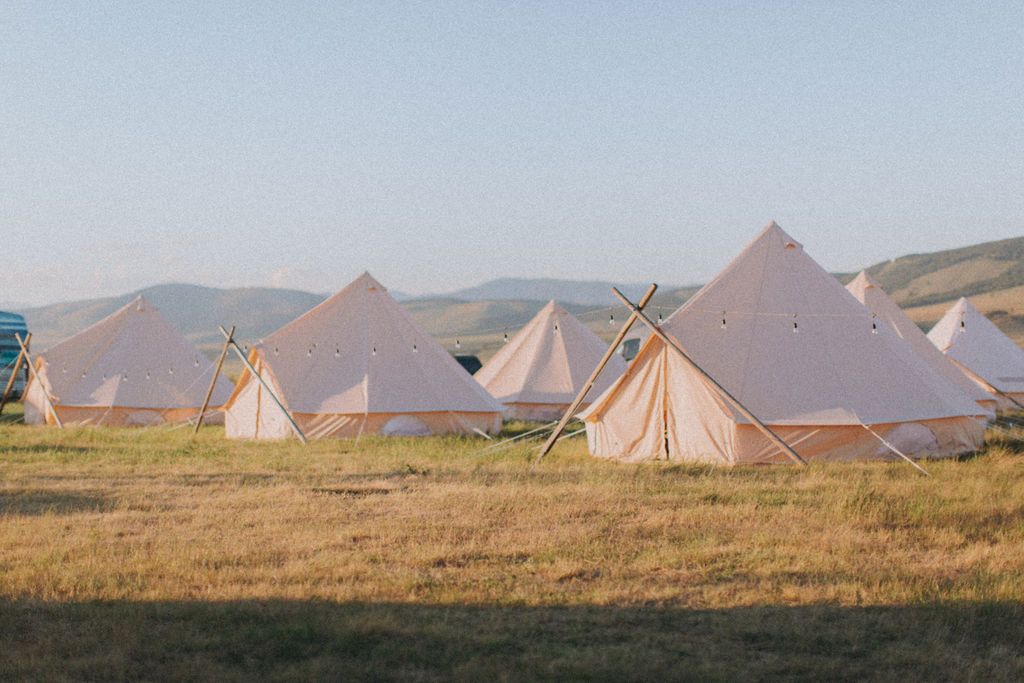 A row of tents are sitting in a field with mountains in the background.