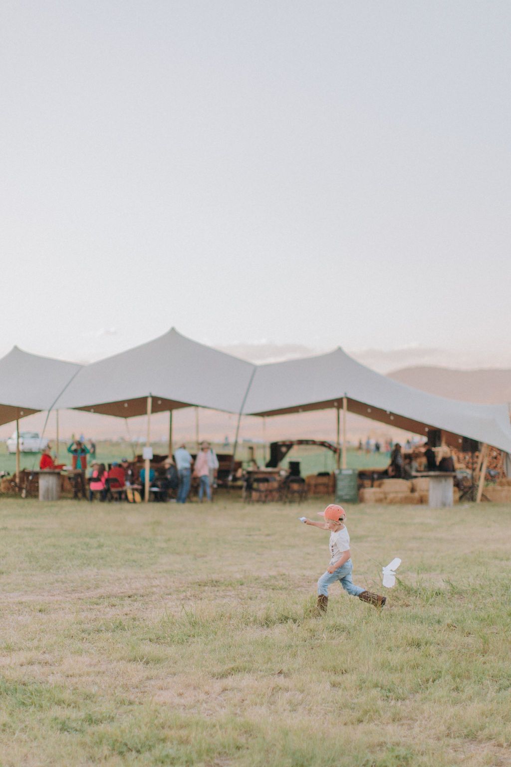 A little boy is running in a field in front of tents.