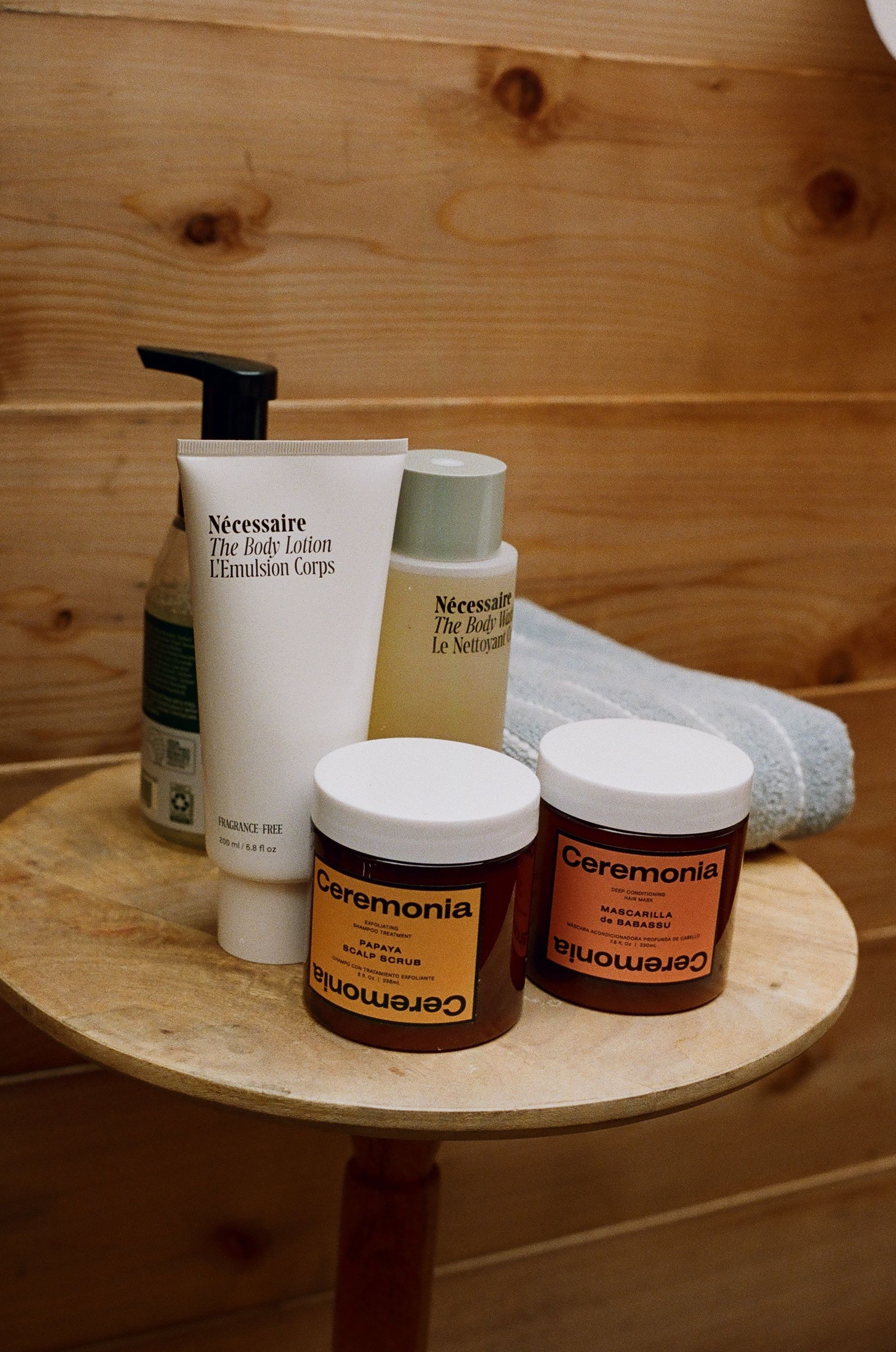A wooden table topped with bottles of cosmetics and a towel.