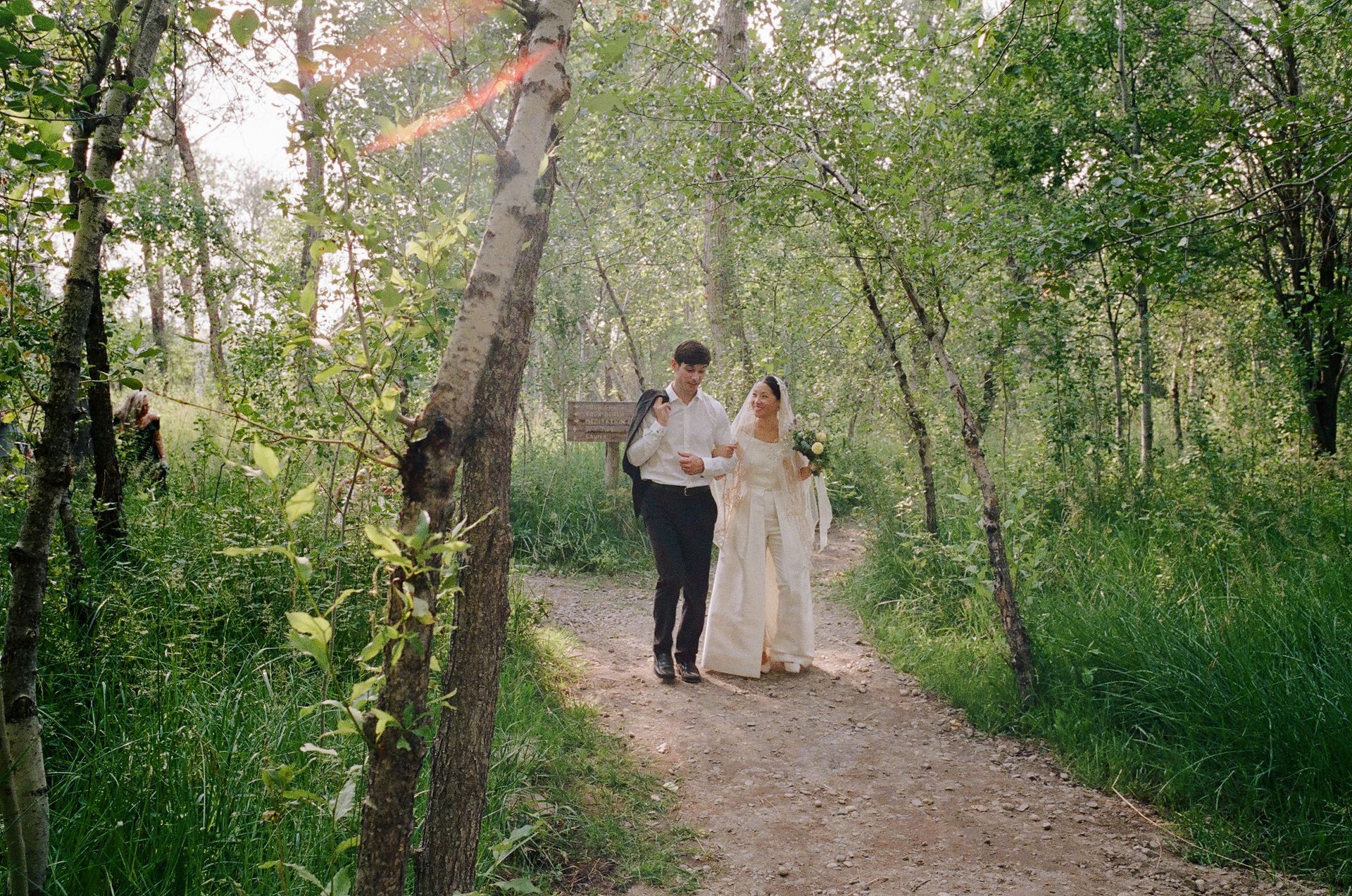 A bride and groom are walking down a path in the woods.