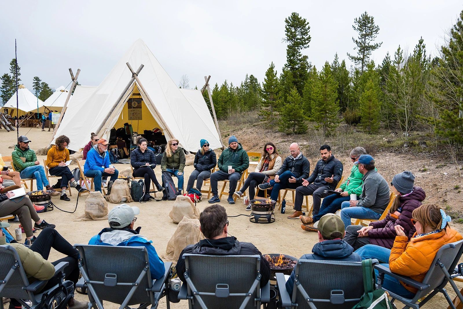 A group of people are sitting around a campfire in front of a tent.