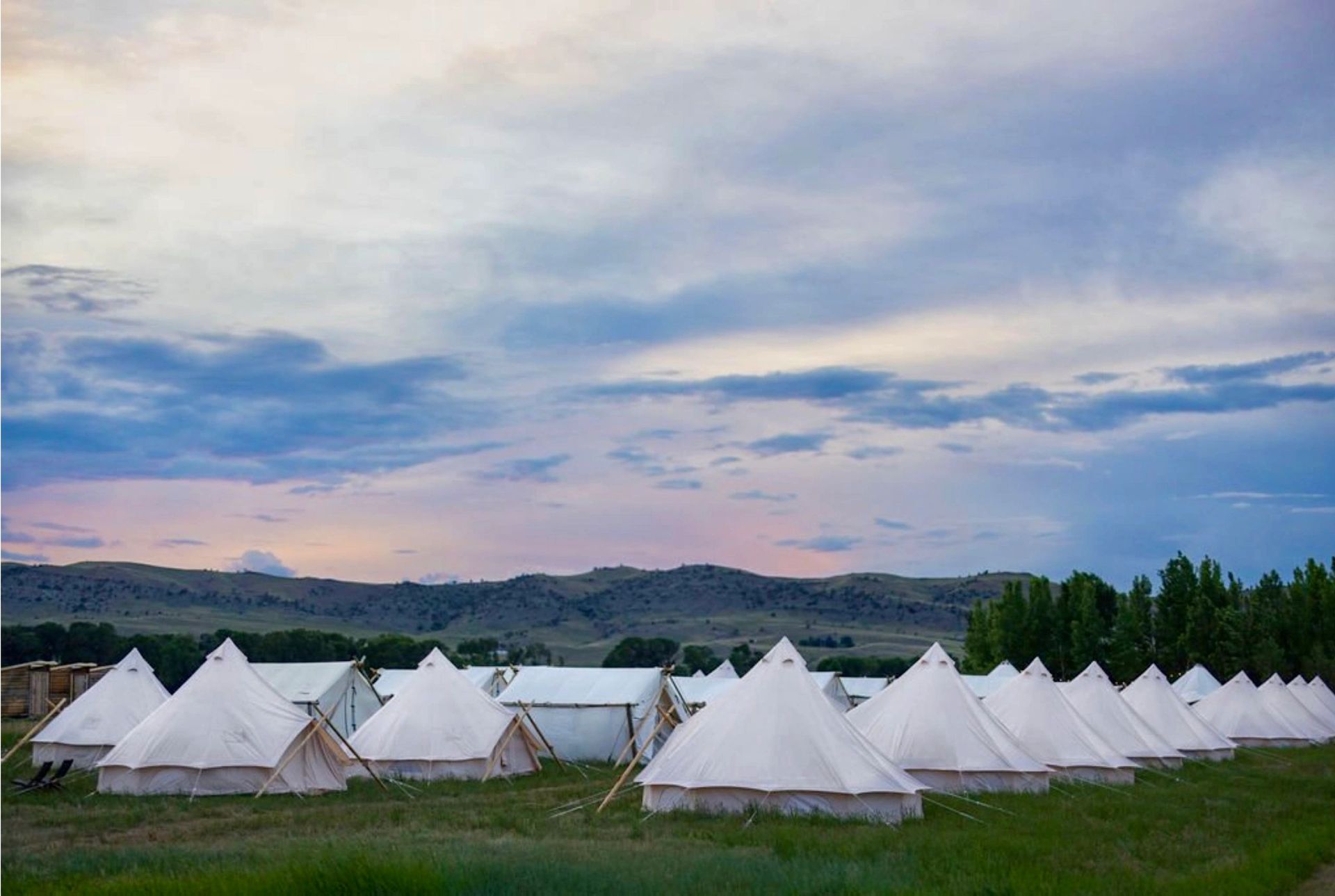 A row of tents in a field with mountains in the background.