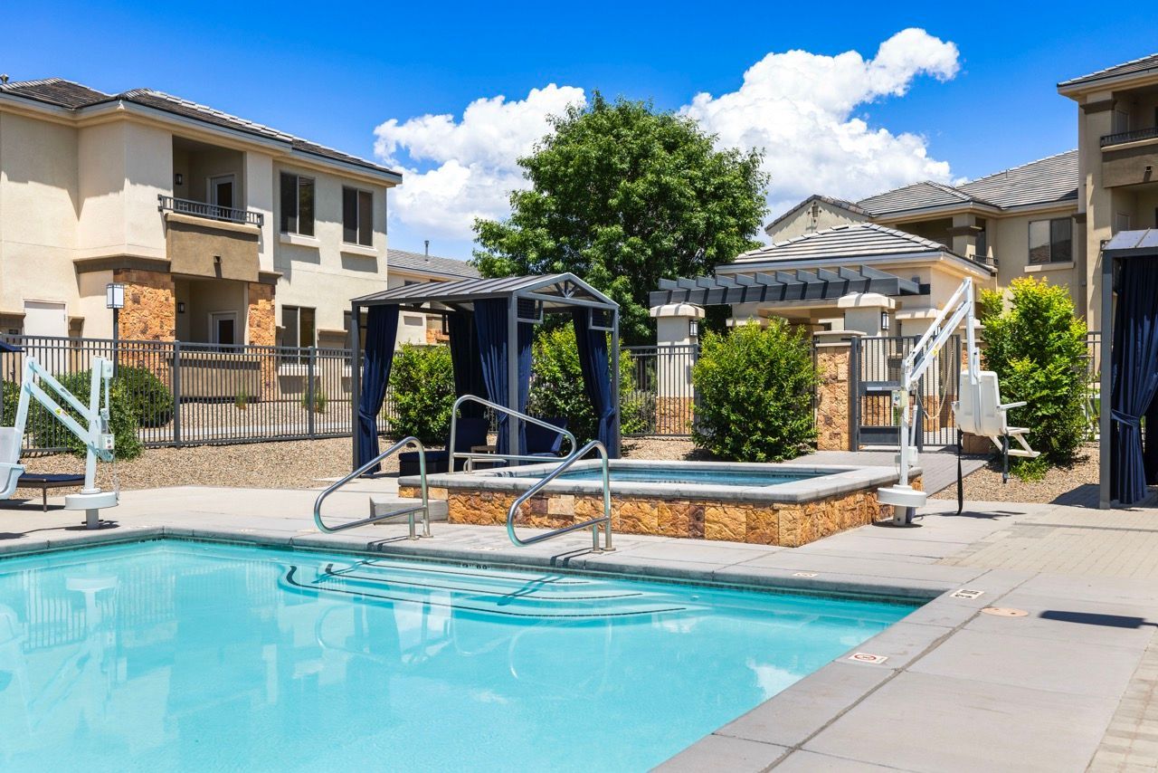 Outdoor community pool area with cabanas, a raised hot tub, and surrounding apartment buildings.