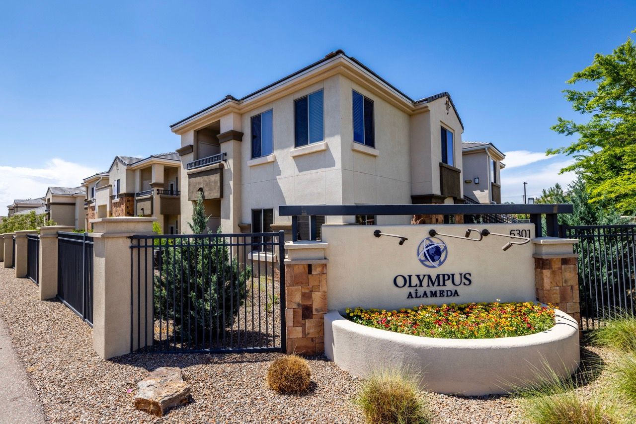 Gated entry to Olympus Alameda apartment community with beige buildings and a landscaped sign.