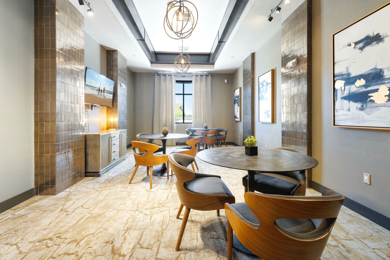 Indoor community lounge with round tables, wooden chairs, wall art, and a large window.