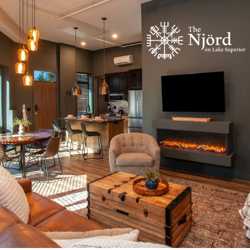 A living room with a couch a chair and a fireplace with the njord logo on the wall