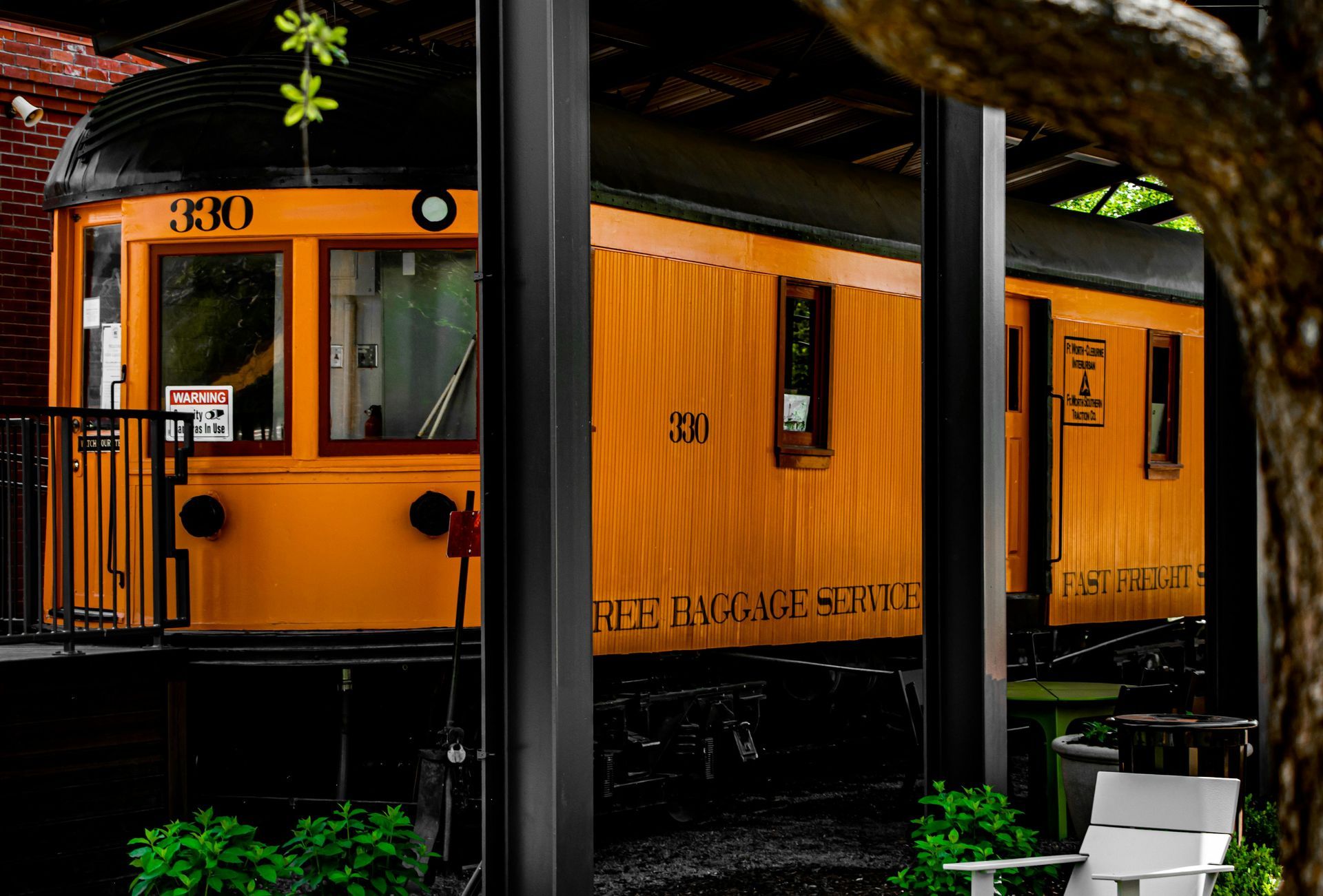 An orange train car is parked under a covered porch.