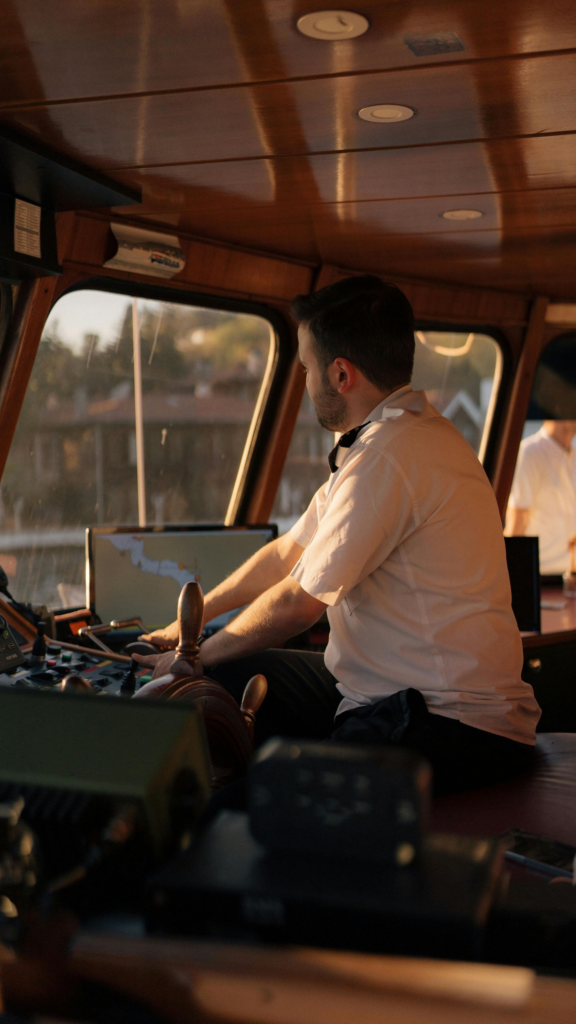 A man is sitting at the steering wheel of a boat.