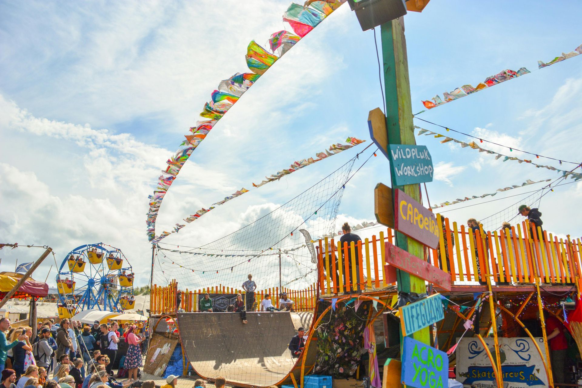 A crowd of people are gathered at a carnival with a ferris wheel in the background.