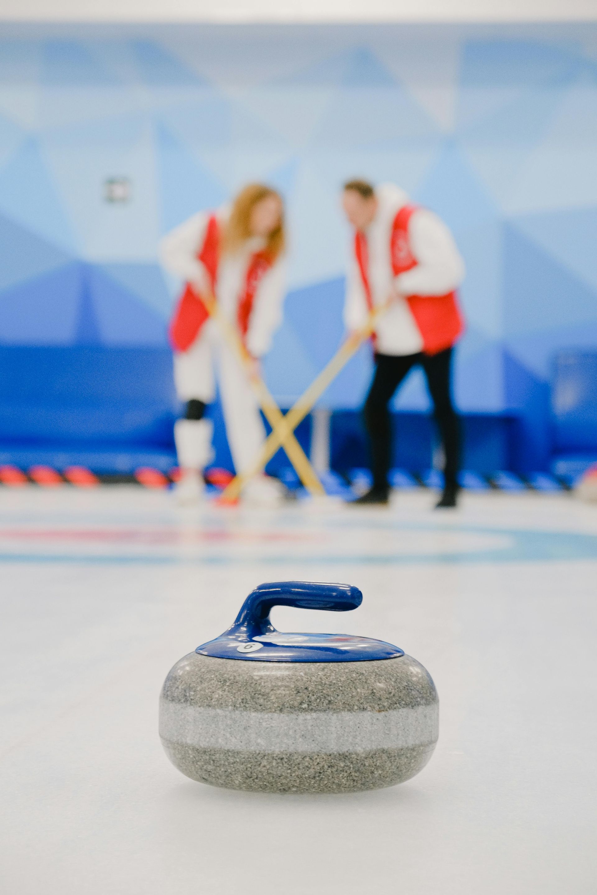 A couple of people are playing curling on a rink with a rock in the foreground.