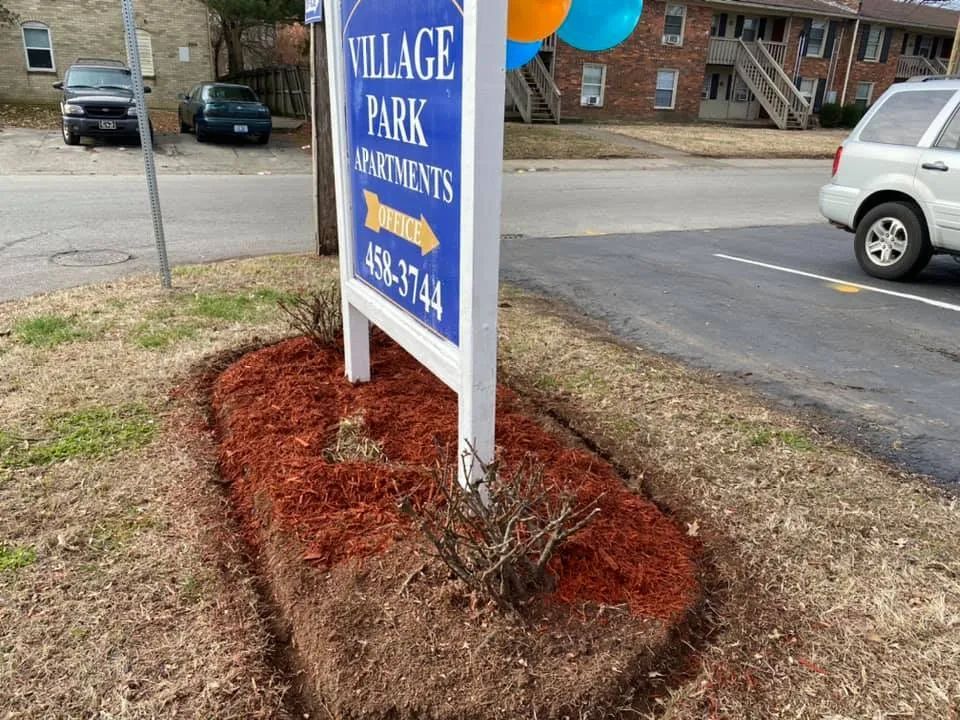 A sign for village park apartments is sitting on the side of the road.