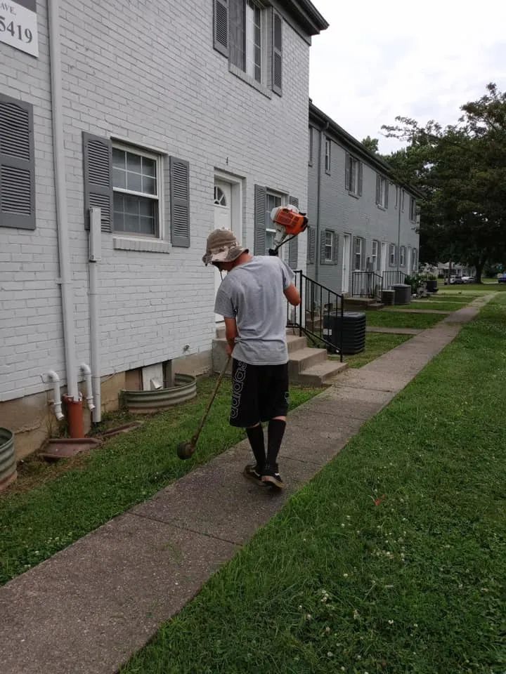 A man is walking down a sidewalk while using a lawn mower.