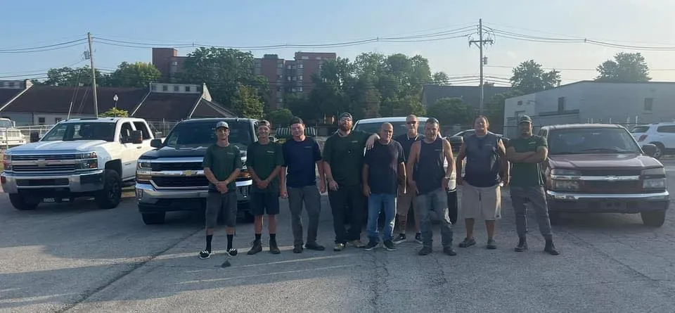 A group of men are standing in front of trucks in a parking lot.