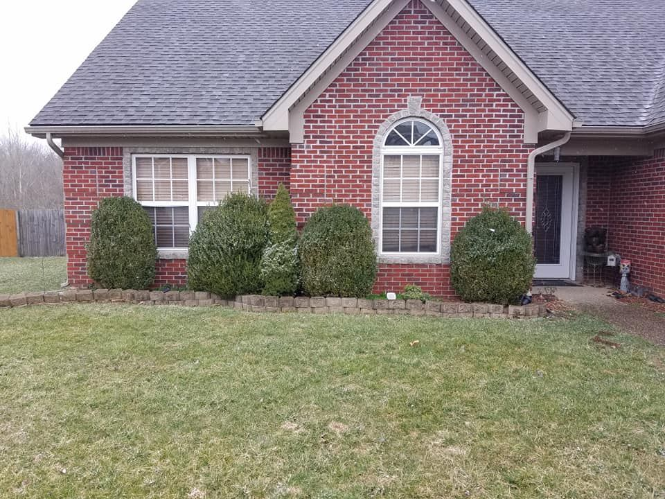 A brick house with a gray roof and bushes in front of it