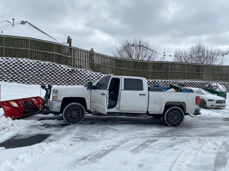 A white truck is parked in the snow next to a snow plow.