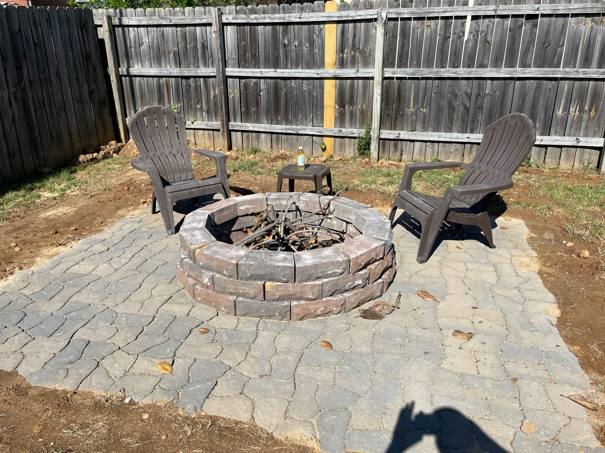 A fire pit with two chairs in front of a wooden fence.