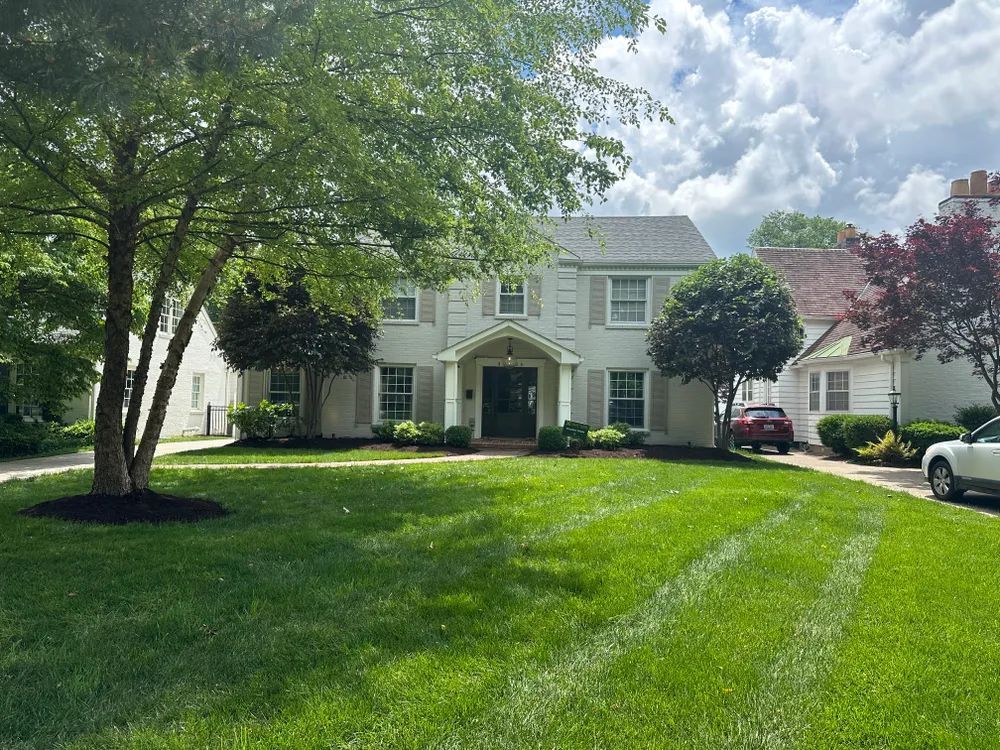 A large white house with a lush green lawn and trees in front of it.
