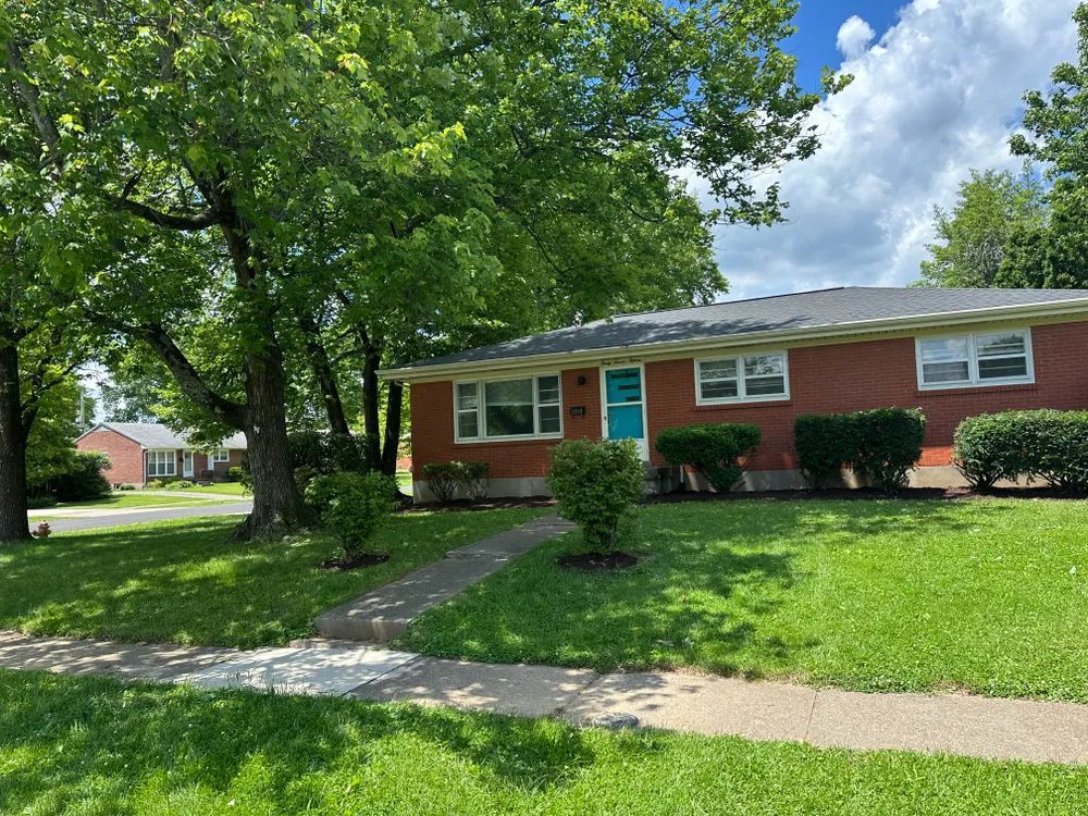 A red brick house with a blue door is surrounded by trees and grass.